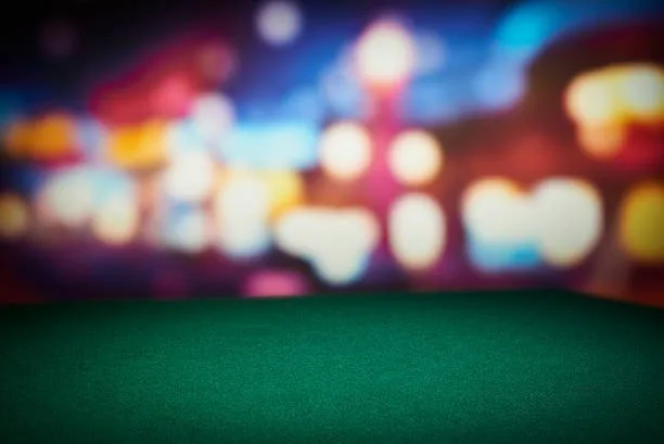 Empty green felt table in front of blurred casino lights